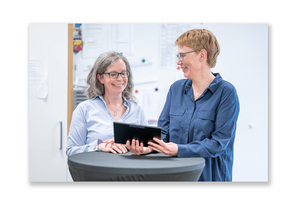 Foto von zwei lachenden Frauen die auf ein Tablet schauen, links steht Eva-Maria Deggerich-Sollert(Akademieleitung) und rechts steht Anja Bergmann (Dozentin)